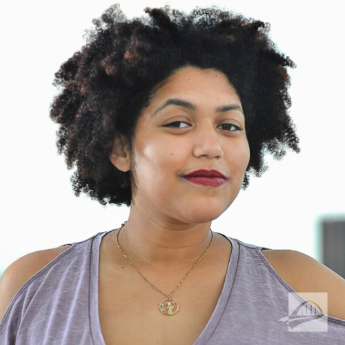 Paige Washington headshot. Paige is wearing a lavender tank top, maroon, lipstick, and a necklace with a pendant. They have short curly brown/black hair. 