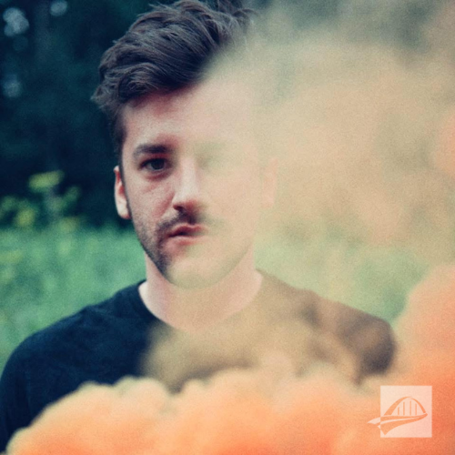 Matthew Smith headshot. Matthew is wearing a dark long sleeved shirt. He has short brown hair and is standing outside in a field where his face is partially covered by a cloud of orange dust.