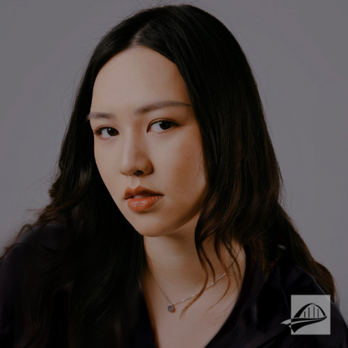 Katherine Chung headshot. Katherine is wearing a black shirt, a dainty chain necklace with a small pendant, has black hair, and is sitting in front of a gray background.